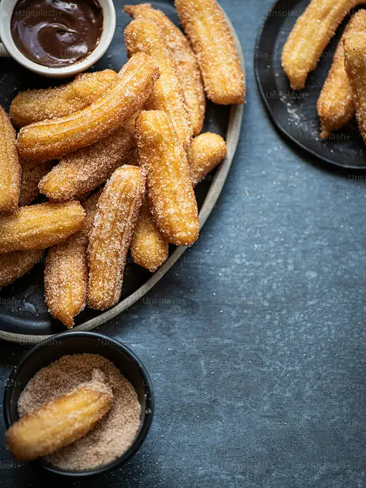 Encimera oscura con tres platos que contienen churros espolvoreados de azúcar y canela