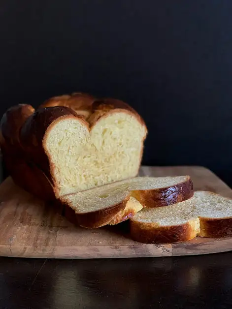 fondo y mesa negro con una tabla de madera que contiene un pan brioche