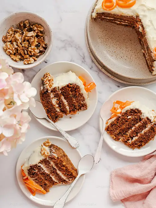 encima de la encimera de mármol se encuentra un cuenco con nueces, tres platos con tres raciones de tarta de zanahoria y un cuarto plato más grande con el resto de la tarta